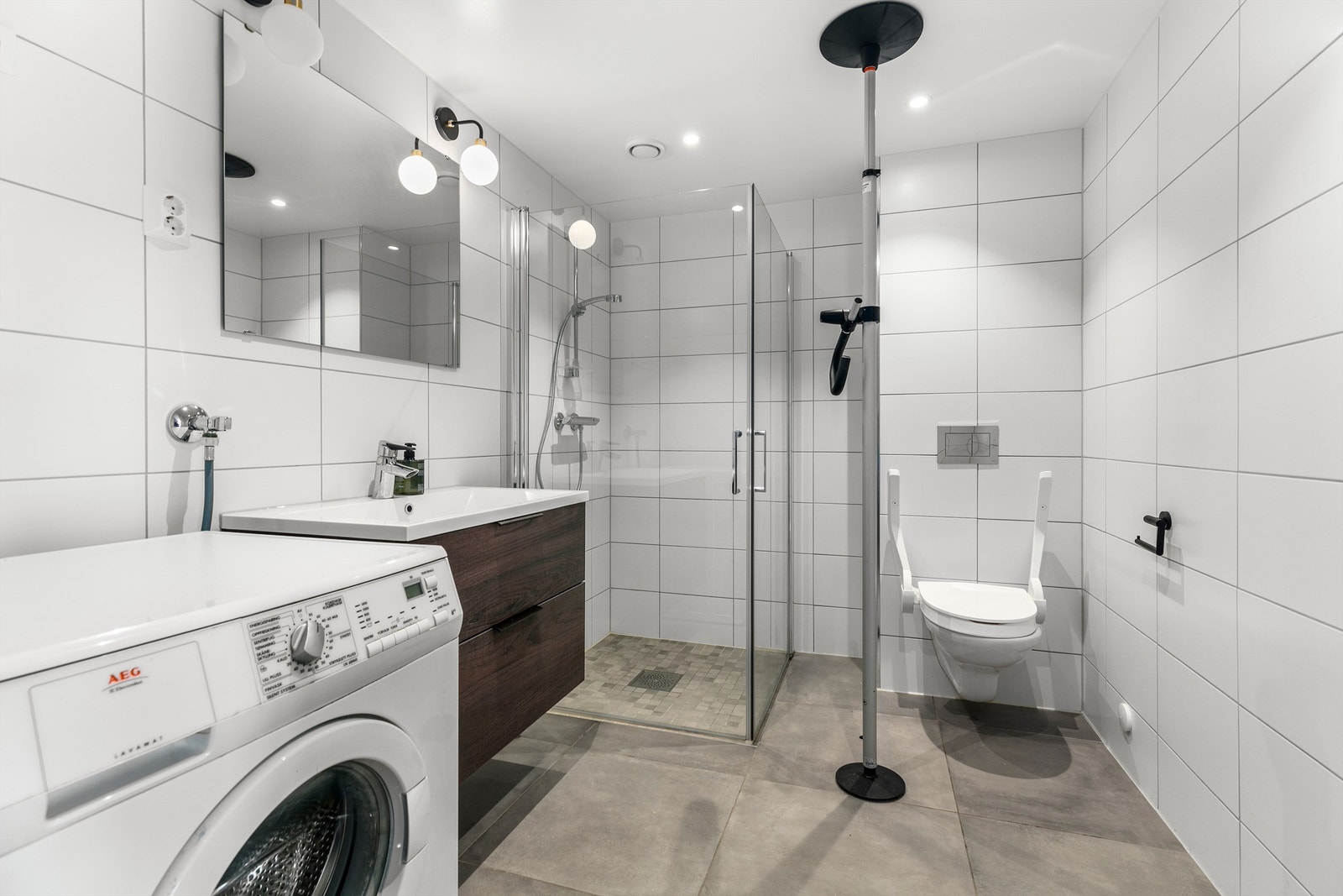 Romslig bad/wc/vaskerom med tidløst fargevalg og moderne baderomsinnredning med underskuffer. Opplegg for vaskemaskin og tørketrommel. Galleribilde