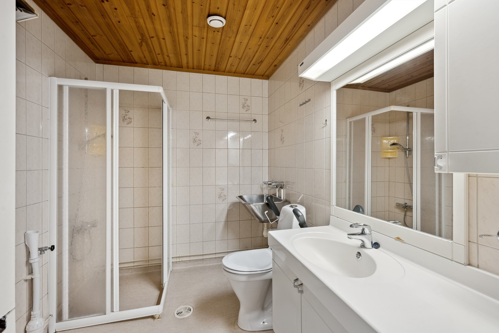 Baderom med flislagte vegger og belegg på gulvet. Rommet varmes opp med stråleovn montert på veggen. Mekanisk avtrekk via himlingsventil, og tilluft via åpen dør. Badet er eldre og bør oppgraderes for å tåle dagens bruk. Galleribilde