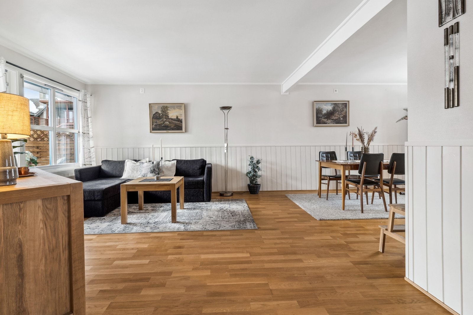Stuen har store vindusflater som gir rommet godt med naturlig lys. Gulv med parkett og vegger med malt brystpanel og glassfiberstrie. Galleribilde