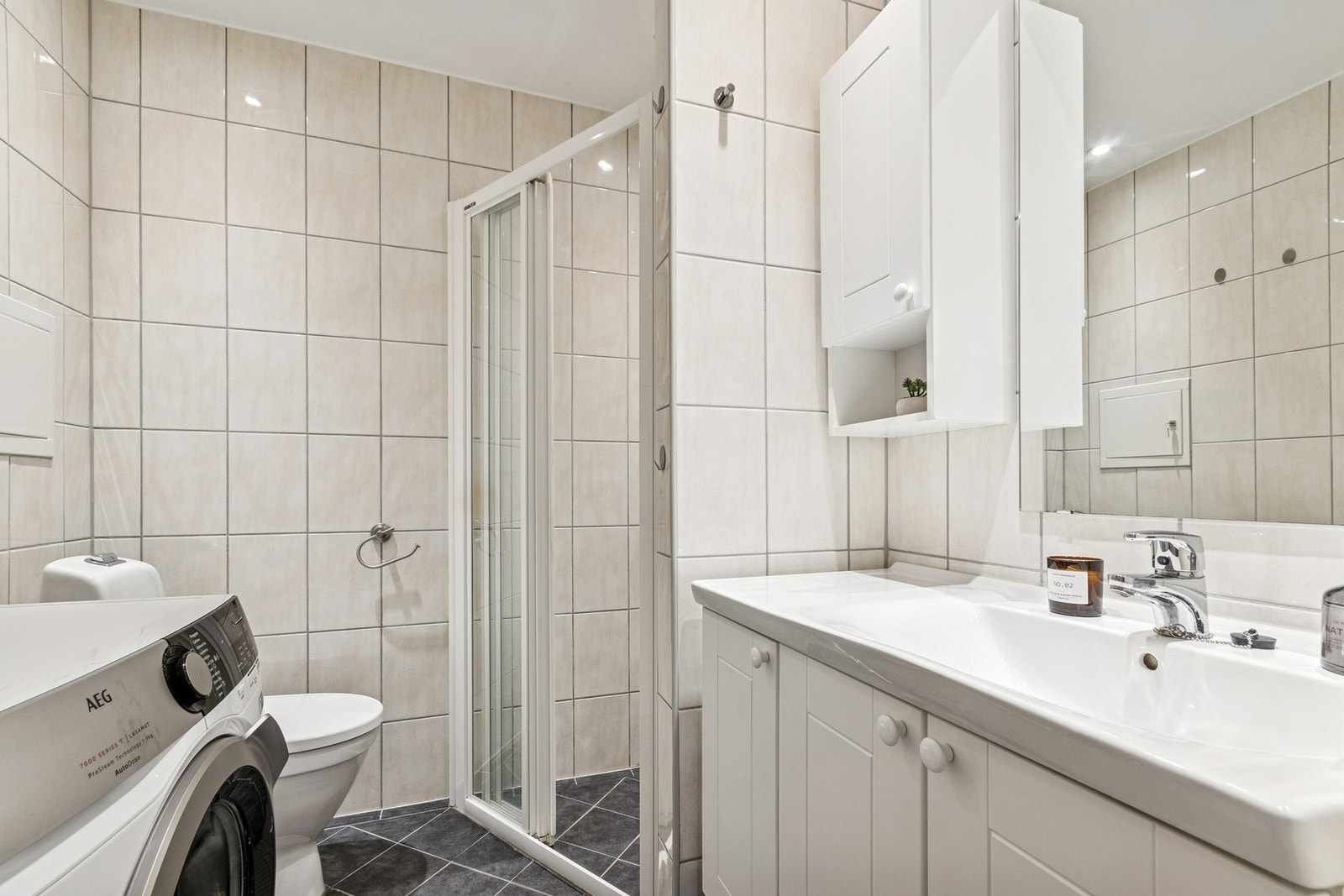 Flislagt baderom med elektriske varmekabler i gulv. Innredning med servantseksjon, WC, dusjnisje - og opplegg for vaskemaskin. Galleribilde