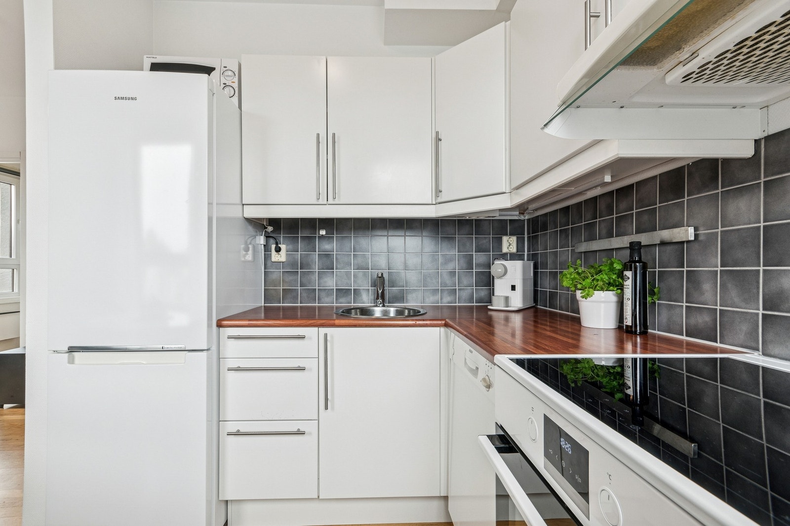 Kjøkken med stilren, hvit innredning og benkeplate i laminat. Frittstående hvitevarer som kan medfølge handelen etter avtale. Galleribilde