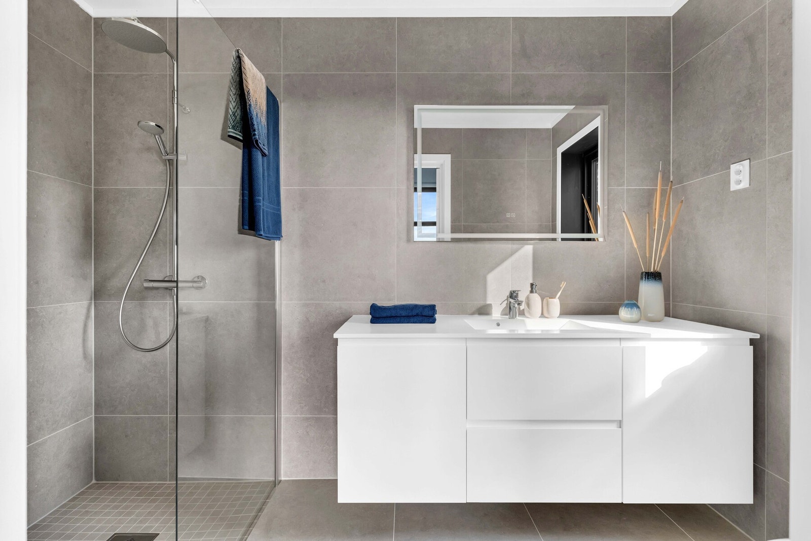 Badet har pene 60x60 fliser på gulv og vegg, i tillegg til servantskap, vegghengt toalett og dusjsone med regnfall. Galleribilde