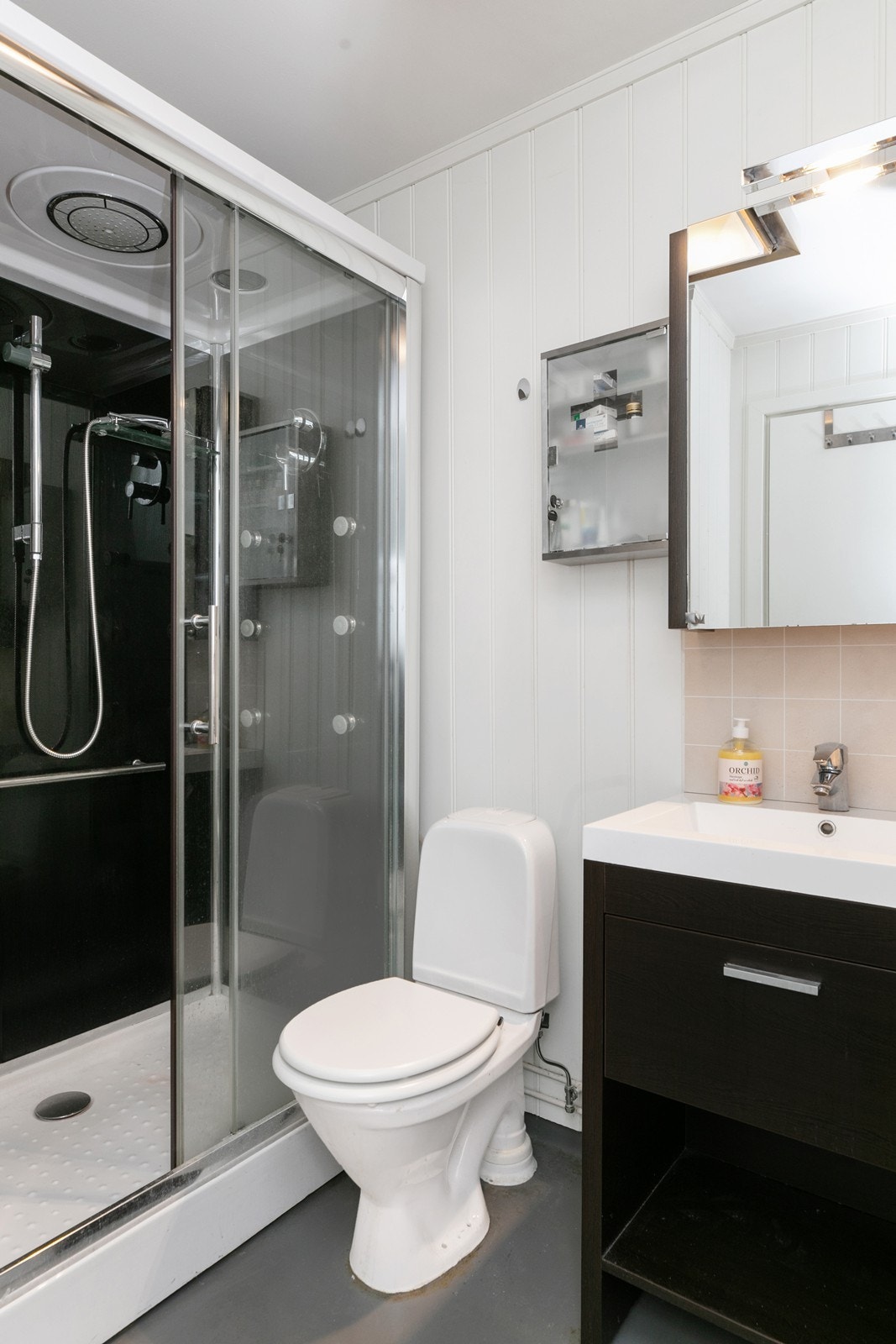 Baderommet har en standard i fra XXXXXXXX med belegg på gulvet og malt panel på veggene. Rommet er utstyrt med gulvmontert wc, servantinnredning med speilskap over, og dusjkabinett Galleribilde