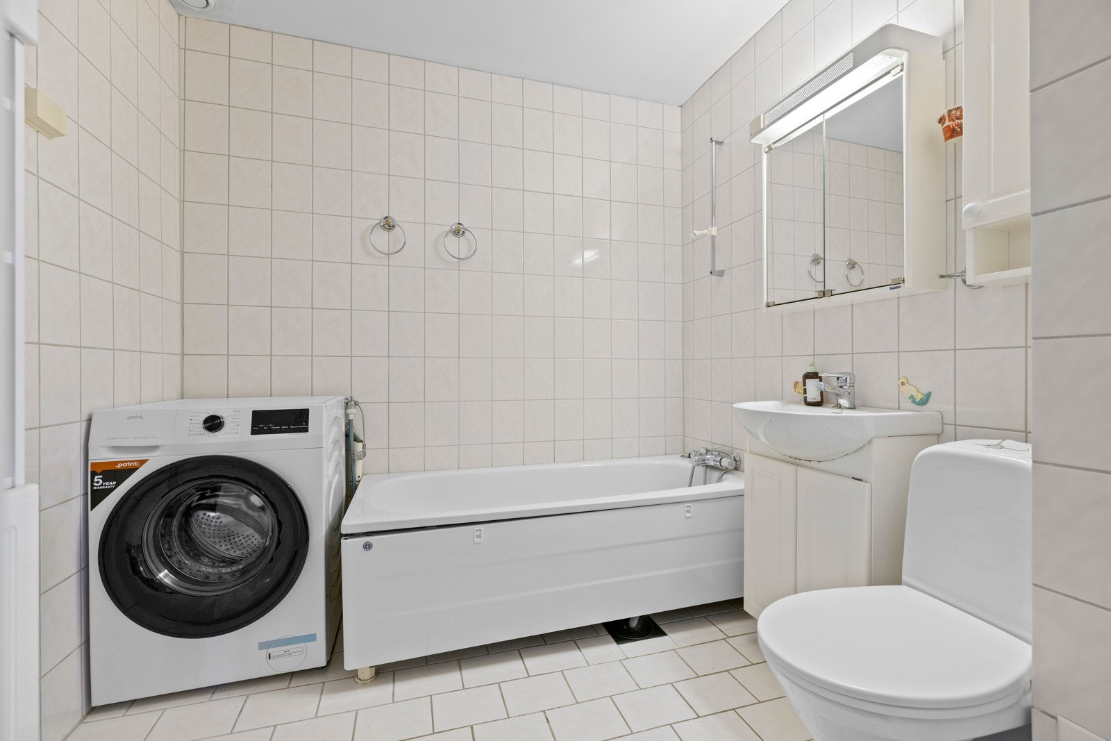 Flislagt bad med varmekabler i gulv. Badet er innredet med badekar, baderomsinnredning med servant, speilskap og toalett. Galleribilde