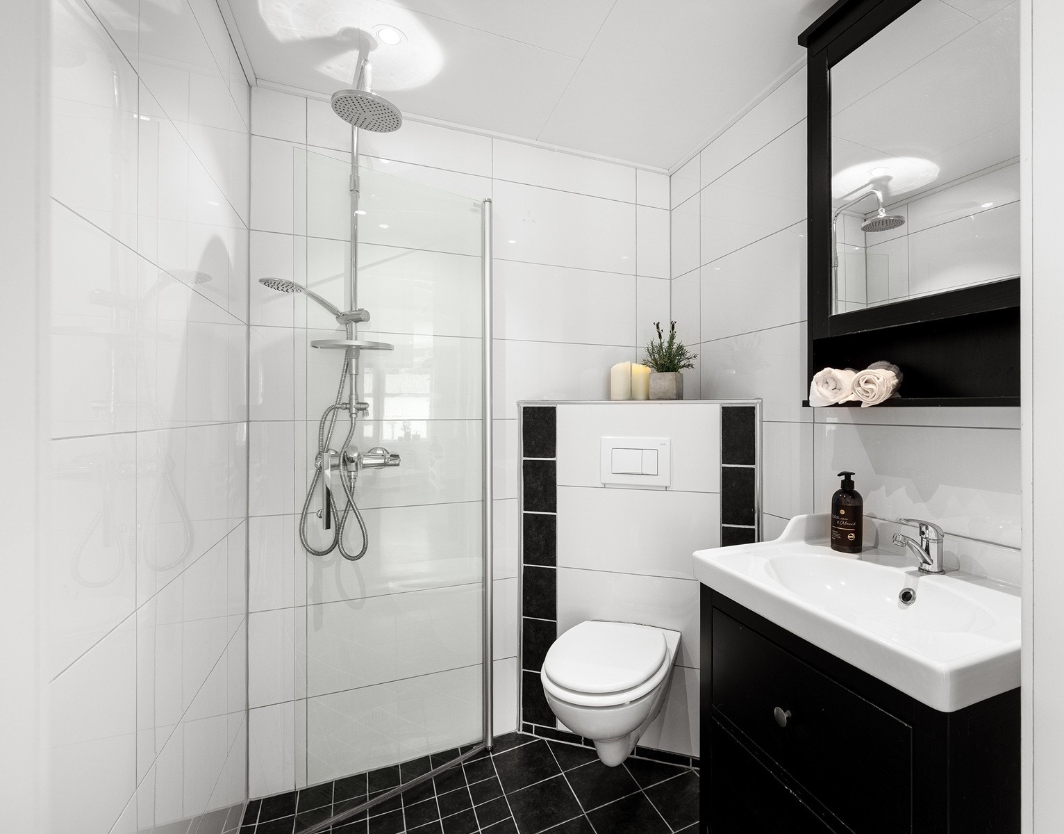 Flislagt bad med moderne kontraster - hvite fliser på veggene, sorte fliser på gulvet og komfortabel gulvvarme. Regnfallsdusj og vegghengt toalett gir et rent og elegant uttrykk. Galleribilde