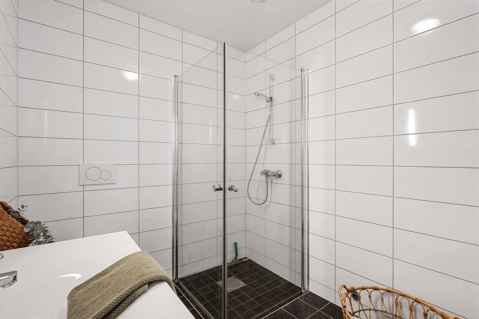 Badet er utstyrt med vegghengt toalett, helstøpt servant, skuffer under servant med slette fronter, dusjdører i klart glass og opplegg for vaskemaskin Galleribilde