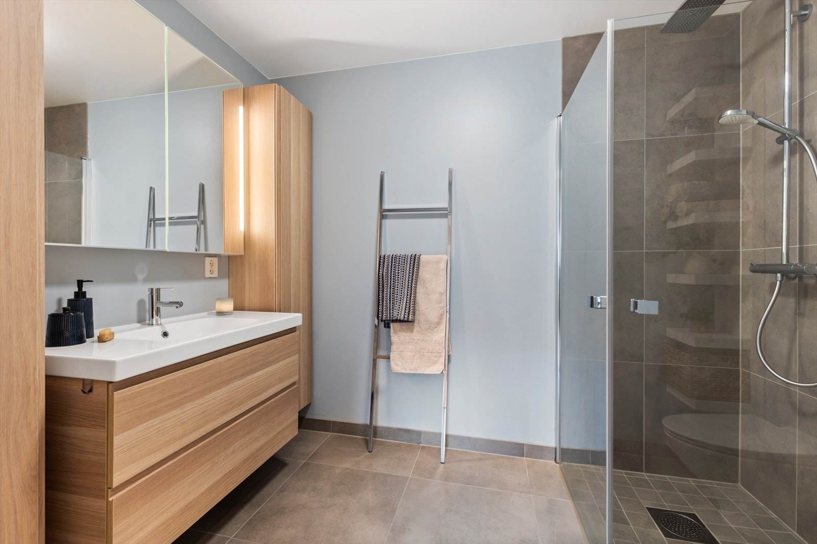 Badet har flislagte gulv med varmekabler. Her er montert romslig innredning med to langskap. Glassdører for dusj kan foldes inn mot vegg. Galleribilde