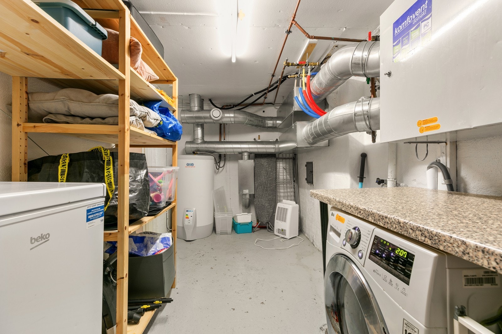 Praktisk vaskerom med opplegg for vaskemaskin, benk, skaper og hyller. Galleribilde