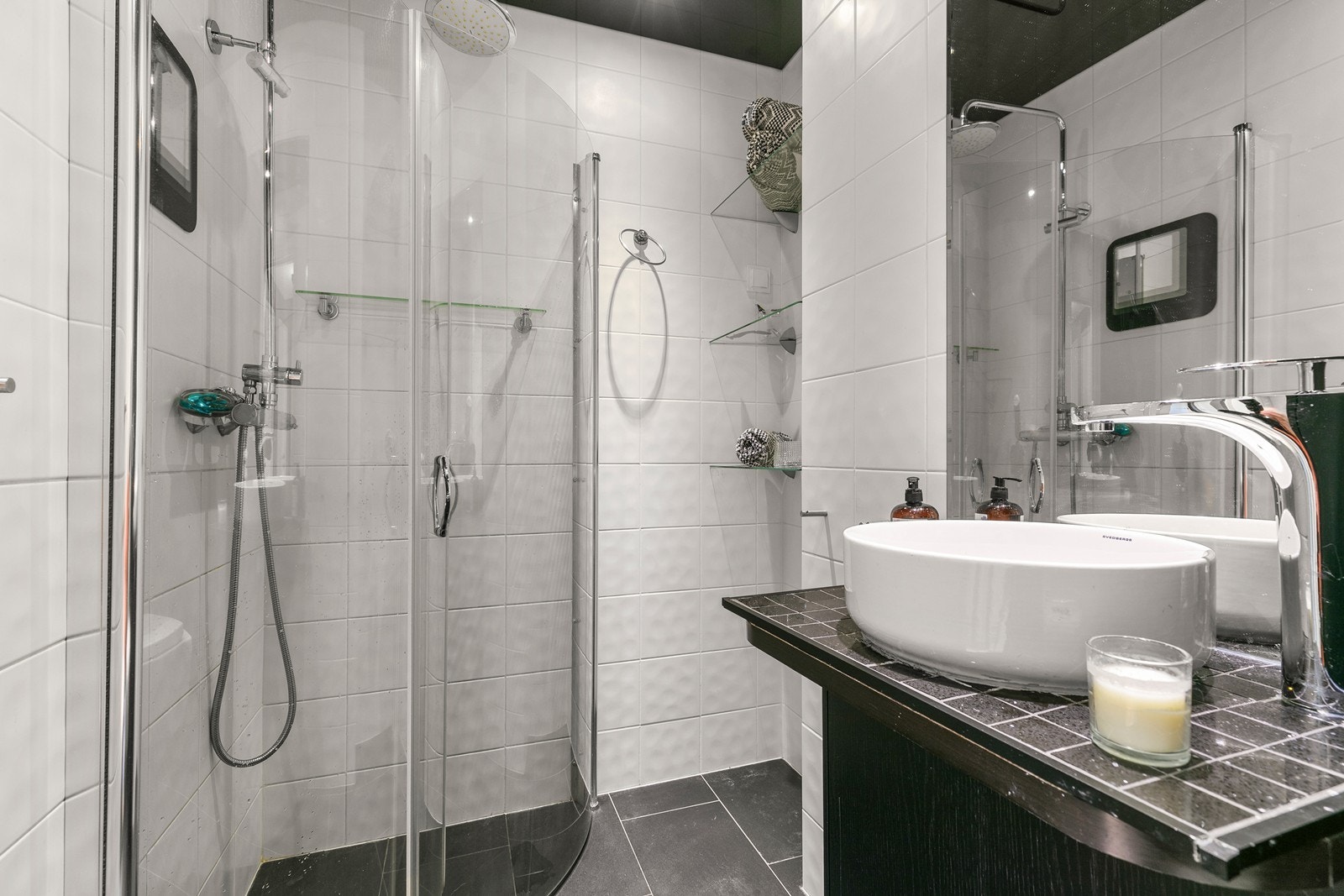 Badet er innredet med rund porselensservant med designarmatur, mørkt servantskap, matchende høyskap og speil. Det har veggmontert toalett og et flott dusjhjørne med innfellbare glassdører og regnfallsdusj. Galleribilde