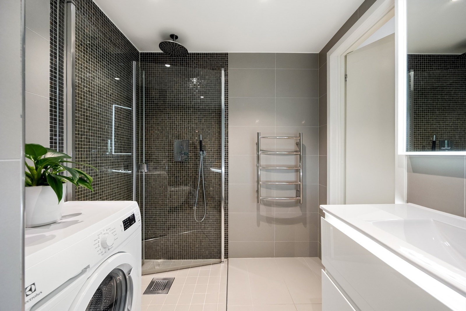 Dusjhjørne med glassdører og dusjarmatur tilkoblet hånddusj og regndusj som gir baderommet et moderne preg. Det er også opplegg for vaskemaskin. Galleribilde