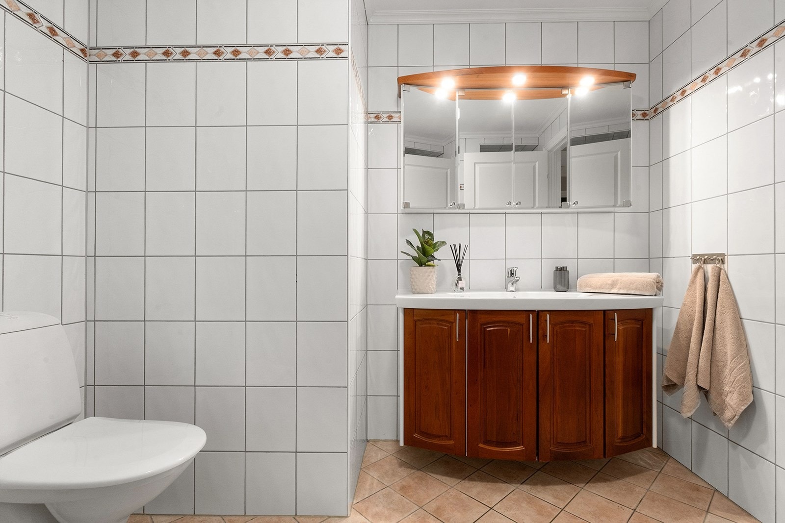 Badet har helfliset gulv og vegger, veggfestet WC og baderomsinnredning med benkeskap og speilskap. Galleribilde