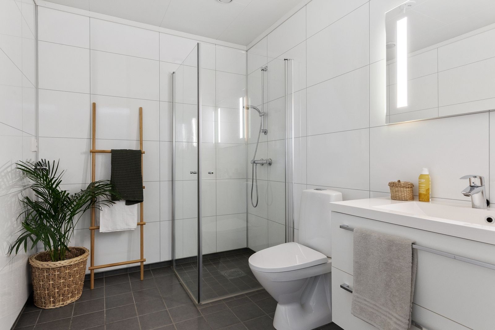 Her er det dusjhjørne med vegger, toalett og innredning med heldekkende hvit vask, underskuffer med slette fronter og speil med lys. Det er opplegg for vaskemaskin og også plass til tørketrommel. Varmekabler i gulv. Galleribilde