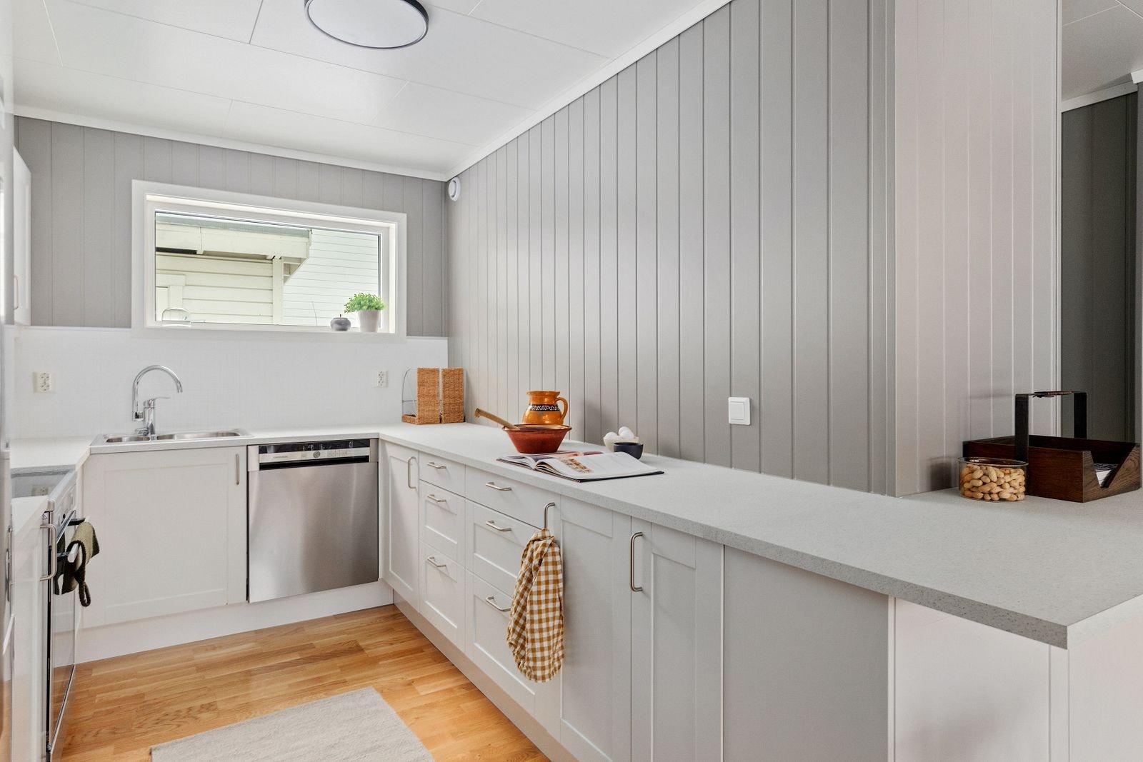 Kjøkkendelen har en pen, hvit innredning med profilerte fronter og laminat benkeplate med nedfelt vask. Galleribilde