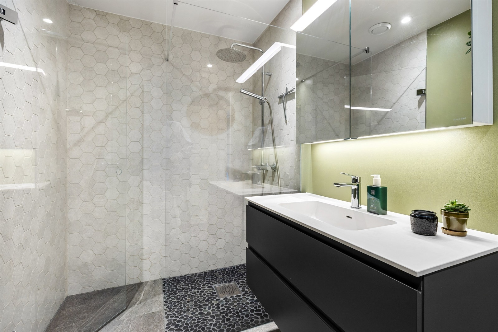 Badet er innredet med servant på servantskap, speilskap med belysning, klosett og dusjhjørne med regndusj. Dusjsonen er flislagt med naturstein for en luksuriøs og spalignende følelse i eget bad. Galleribilde