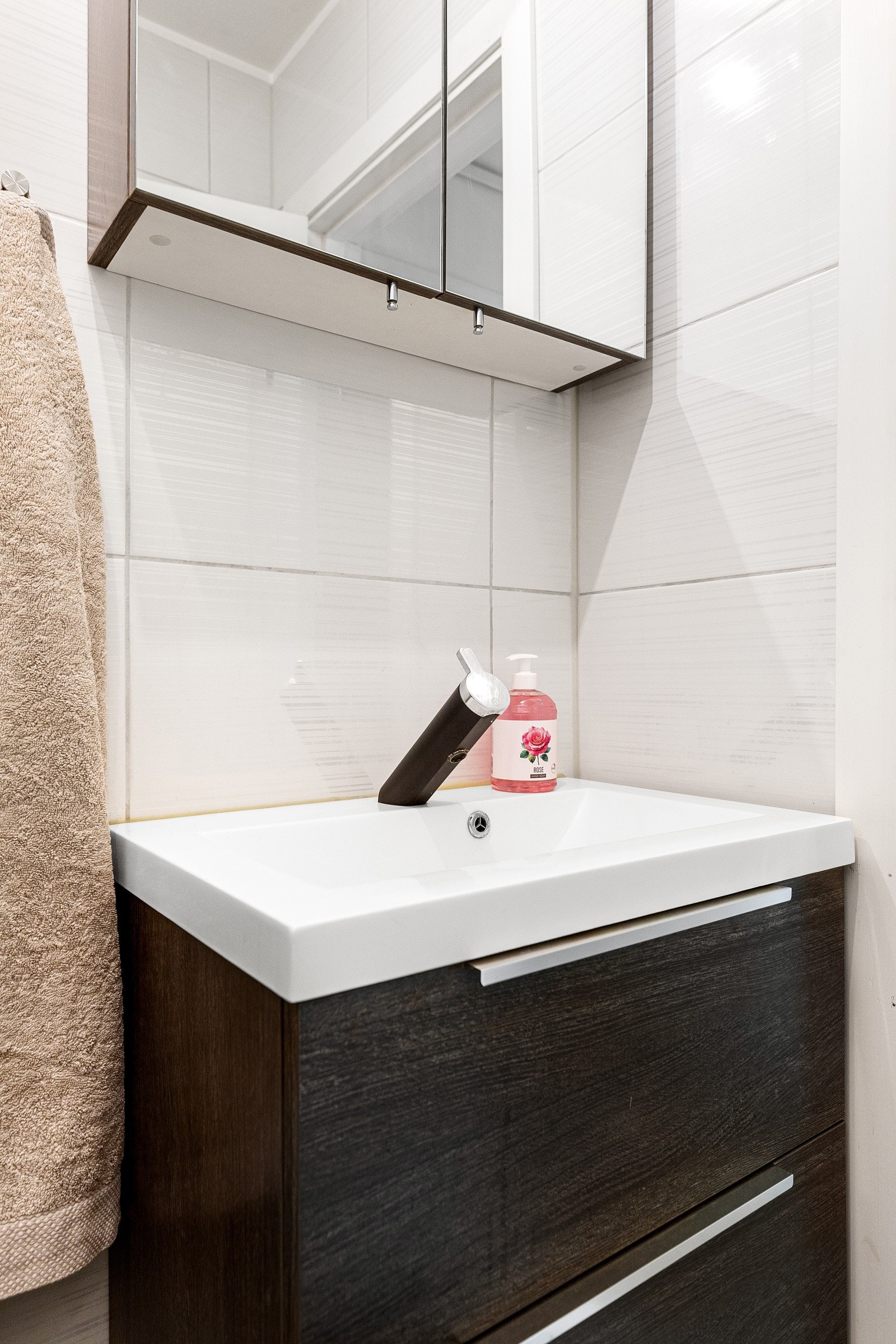 Rommet har innredning med nedfelt servant med underskap i mørk trefarge og speilskap over, toalett og dusjhjørne Galleribilde