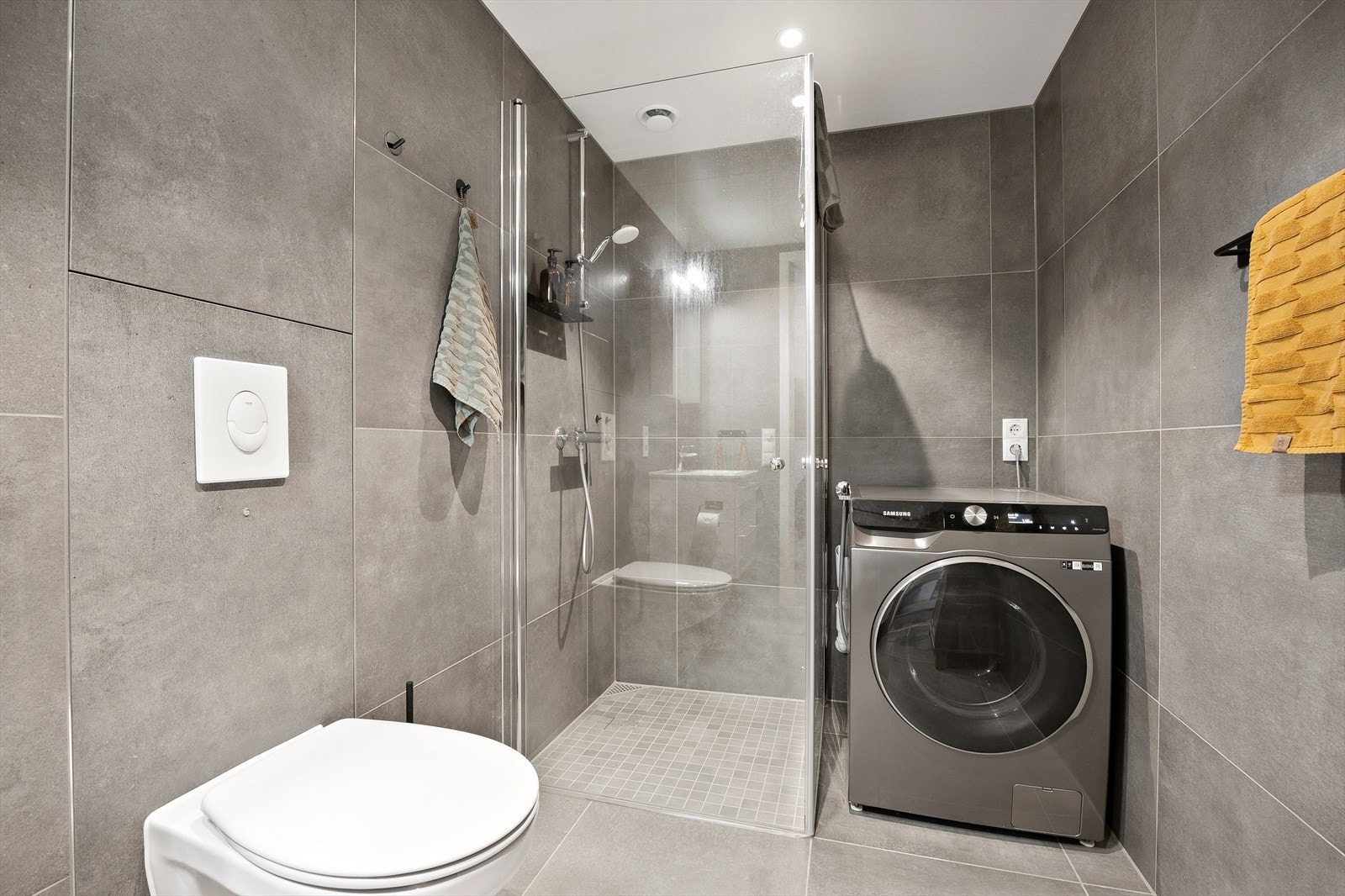 Det er nedfelt servant i baderomsinnredning, veggmontert toalett, dusjvegger/hjørne og opplegg for vaskemaskin. Galleribilde