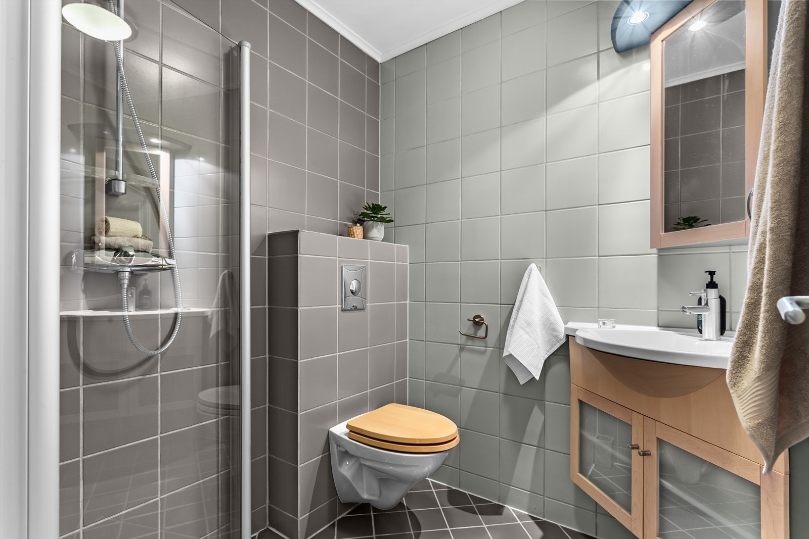 Bad på første plan er innredet med innredning fra Dansani i lønnetre og stål, sammenslagbare dusjvegger i glass, vegghengt wc og gråtonede fliser med varmekabler. Galleribilde