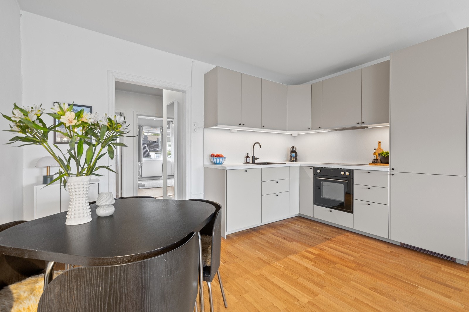 Innredningen består av slette gråbeige skuffe- og skapfronter i kombinasjon med laminert benkeplate i lyst design. Den nedfelte vasken i sort kompositt gir et tidløst preg. Galleribilde