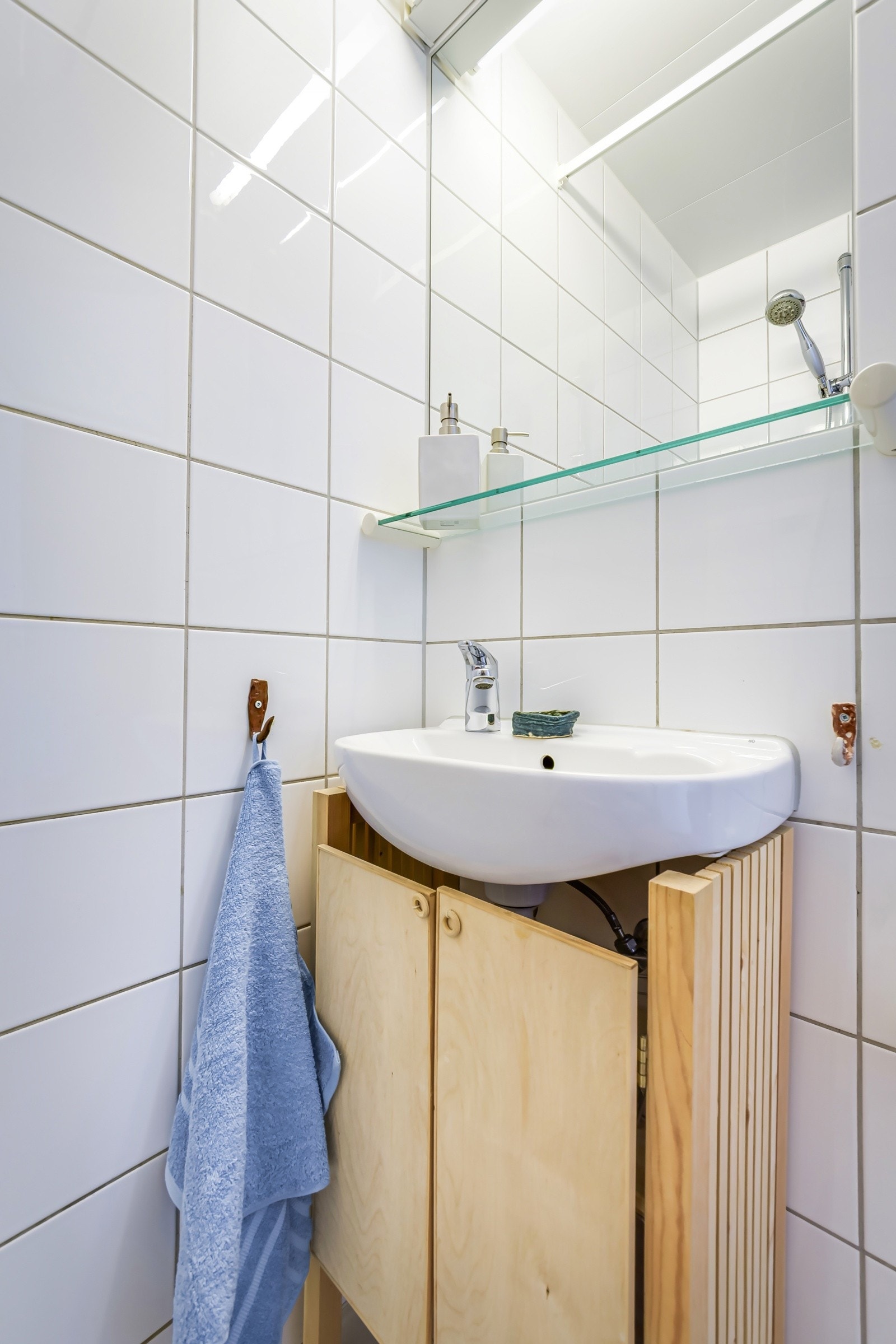 Baderommet er utstyrt med vegghengt servant, speil med glasshylle og belysning over, dusjhjørne med forheng og gulvmontert toalett. Galleribilde