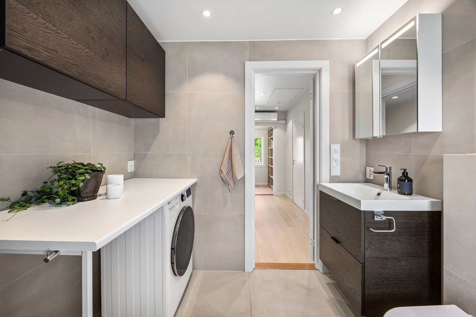 Baderommet er videre utstyrt med servant med innredning, speil og belysning over servant, veggfestet klosett, dusj med innfellbare dører, badekar og veggskap Galleribilde