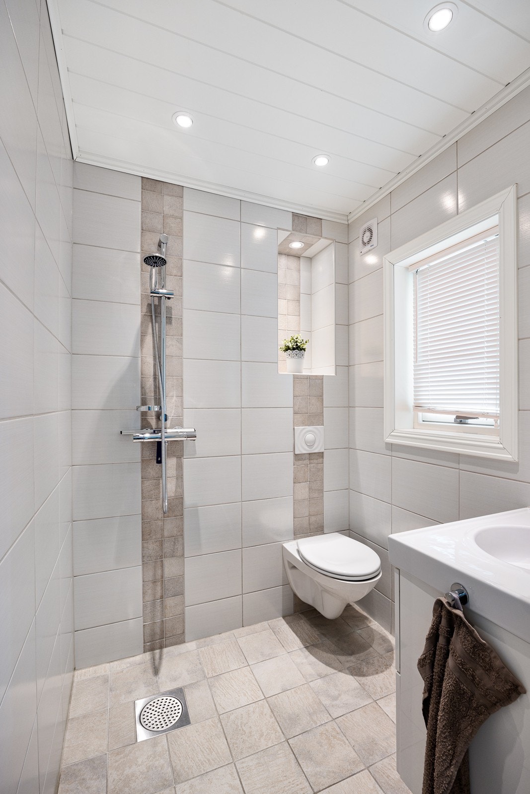 Badet i første etasje ligger i suiteløsning med hovedsoverommet og gir et delikat inntrykk med flislagte overflater, gulvvarme, downlights og elektrisk styrt vifte. Galleribilde