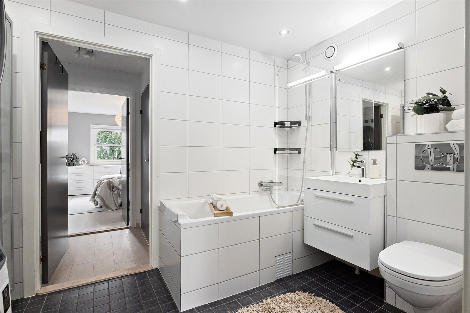 Stilrent hovedbad med badekar, dusjløsning, vegghengt toalett og servant med underskap. Galleribilde