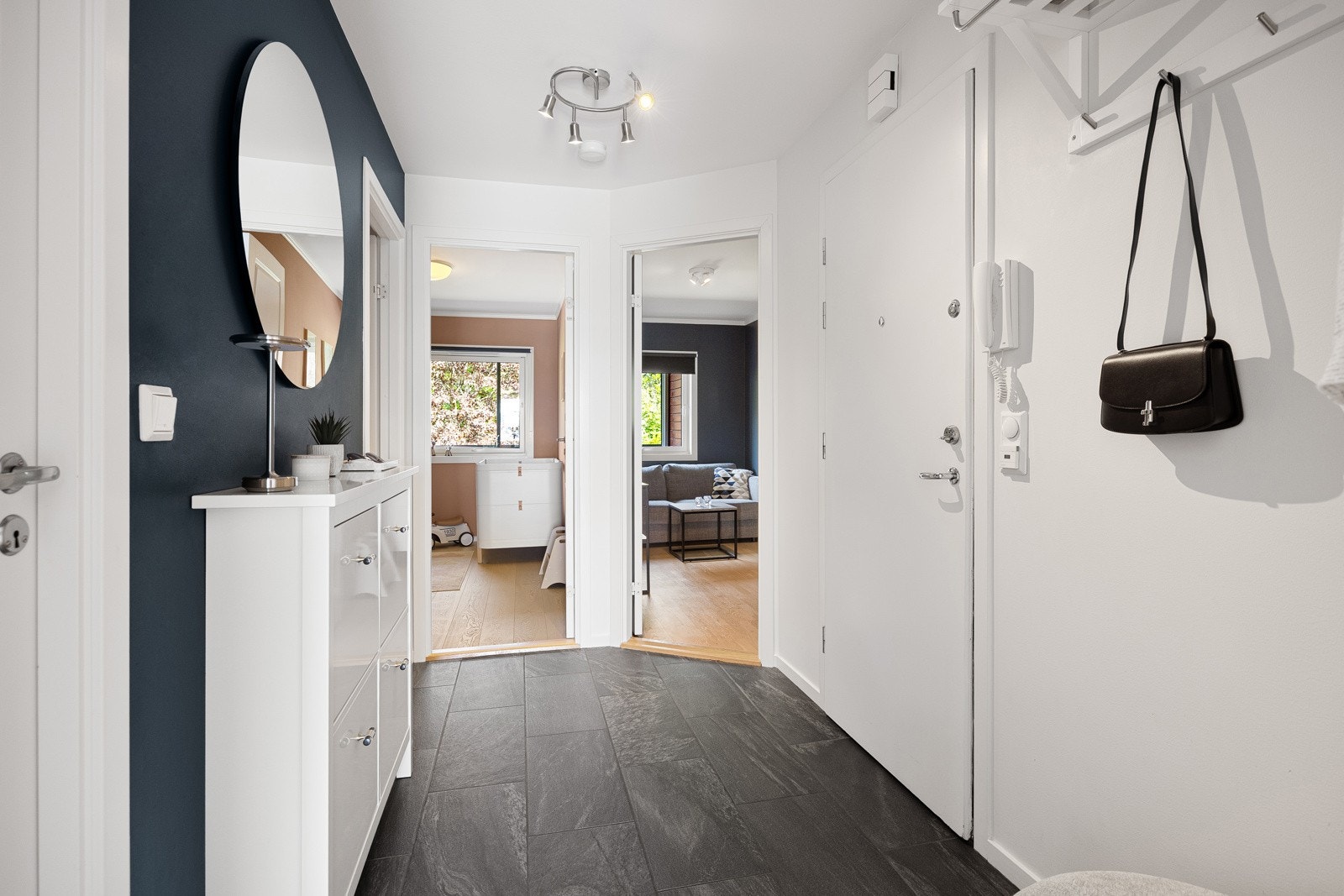 Entreen er innbydende med mørke fliser på gulvet, lysmalte vegger og en dempet, blå fondvegg. Galleribilde