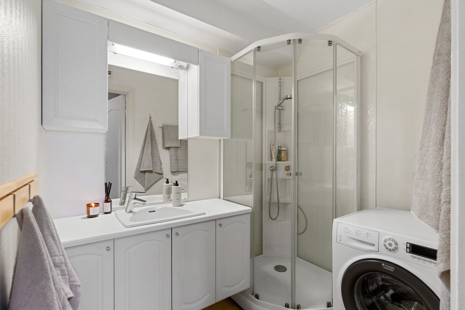 Baderomsinnredningen har hvite fronter og består av en servant på en hylleseksjon og et stort speil med god belysning. Galleribilde