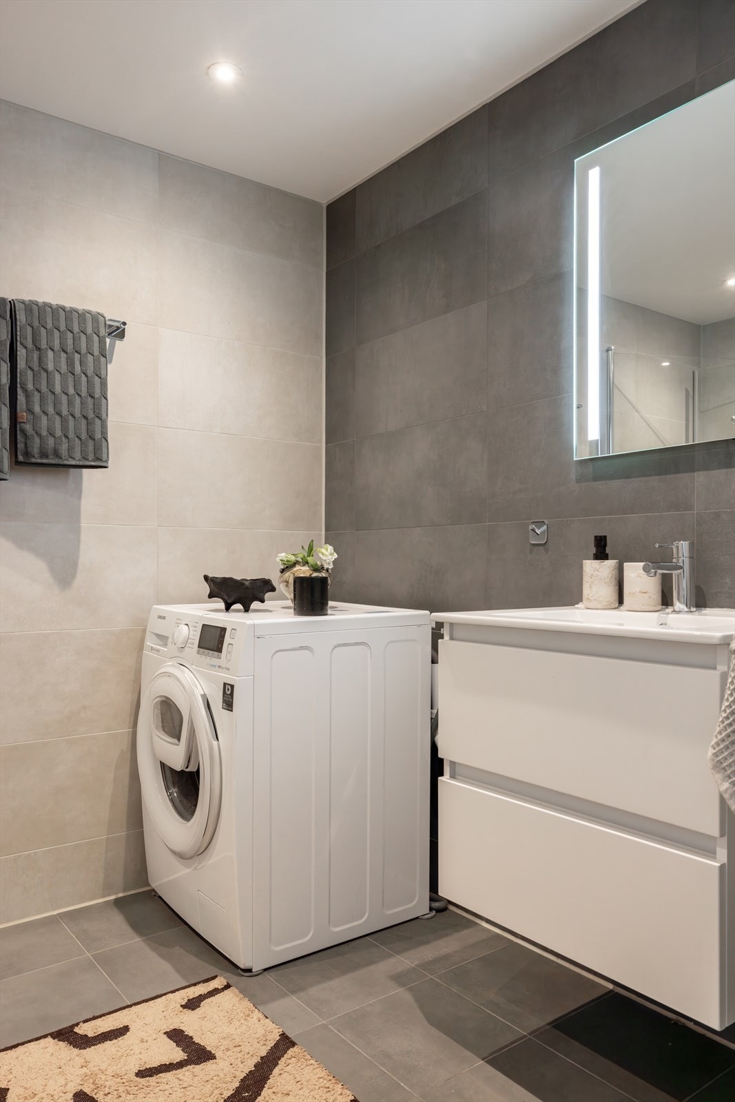 Badet er innredet med heldekkende servant med underskap, speil med belysning og dusj med glassvegger i herdet glass. Opplegg for vaskemaskin/tørketrommel i hjørnet. Galleribilde