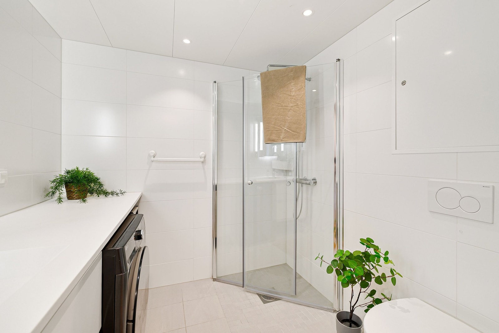 Badet er utstyrt med vegghengt toalett, servantinnredning og dusjhjørne med glassdører, samt opplegg for vaskemaskin eller kombinert vask og tørk. Galleribilde