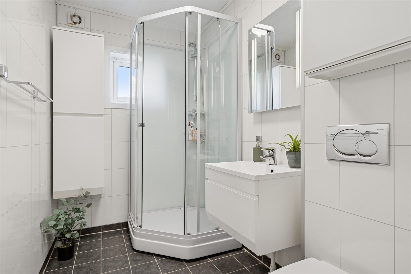 Baderom med fliser på gulvet og baderomsplater på veggene. Dusjkabinett, servant med skuff og veggmontert toalett. Galleribilde