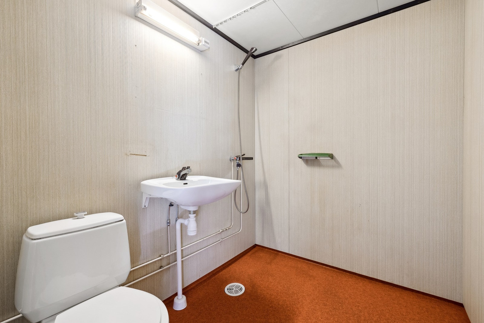 Bad fra byggeår med gulvstående toalett, dusj på gulv og vegghengt servant Galleribilde