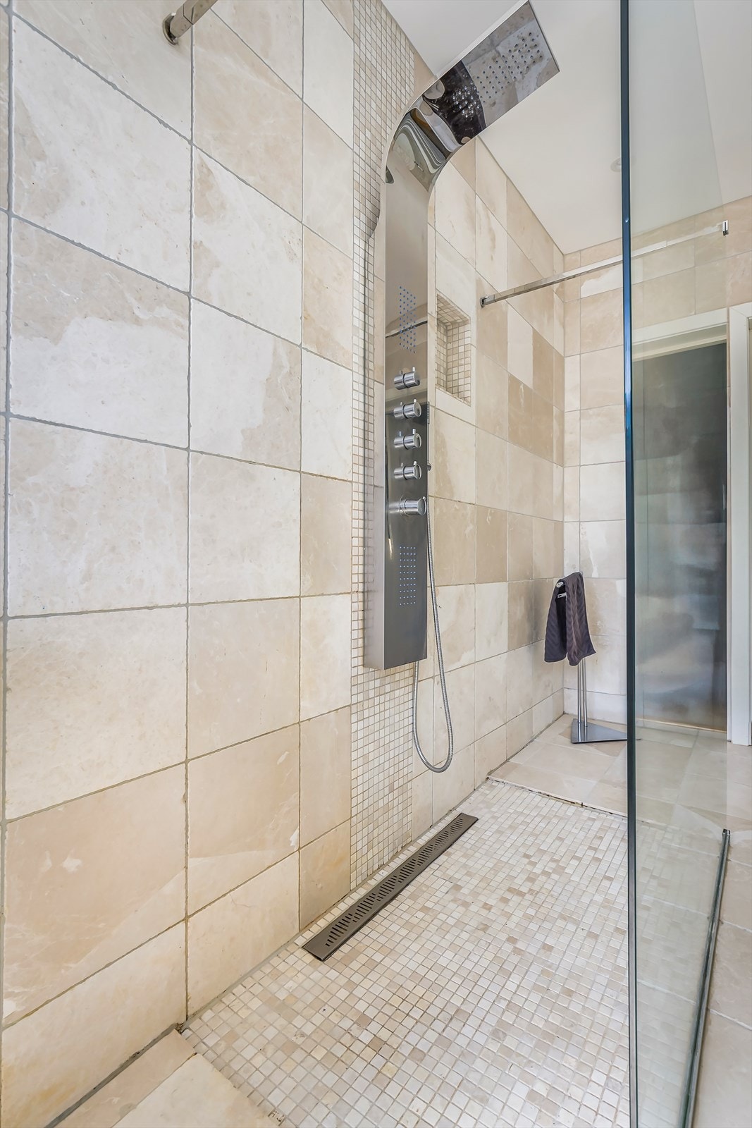 Dusj med mosaikkfliser og glassvegg på midten, badekar med massasje dyser og vegghengt wc. Galleribilde