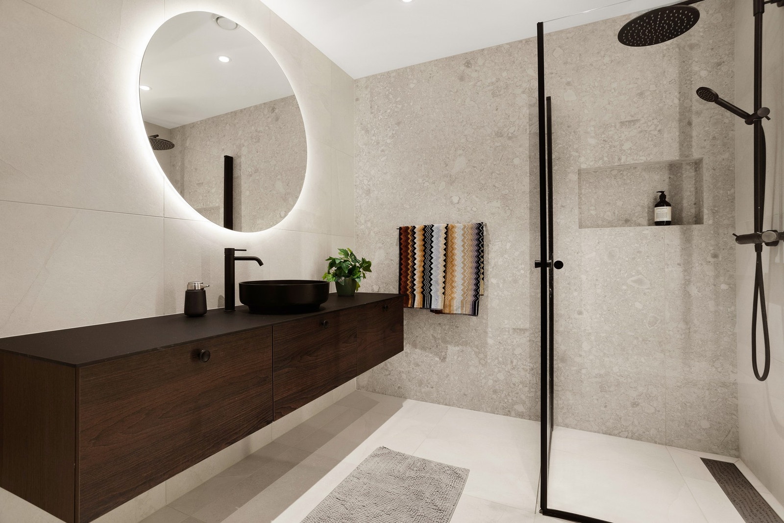 Servantskål oppe på romslig baderomsinnredning, veggmontert spyletoalett og dusjnisje med glassdører. Galleribilde