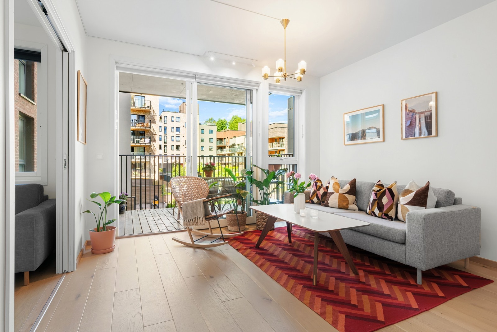 Lys stue med store vinduer og balkong som gir utsikt mot nydelig bakgård. Galleribilde