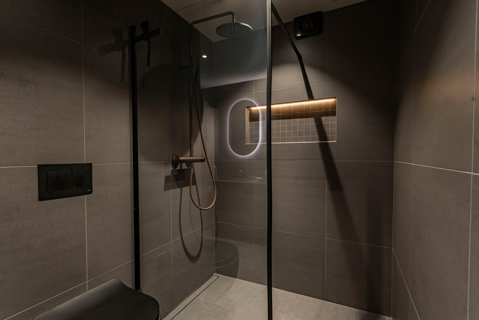 Videre inneholder badet vegghengt toalett med innebygget sisterne og dusj på gulv i hjørnet med glassvegg, hånddusj og regnfallsfunksjon. Galleribilde