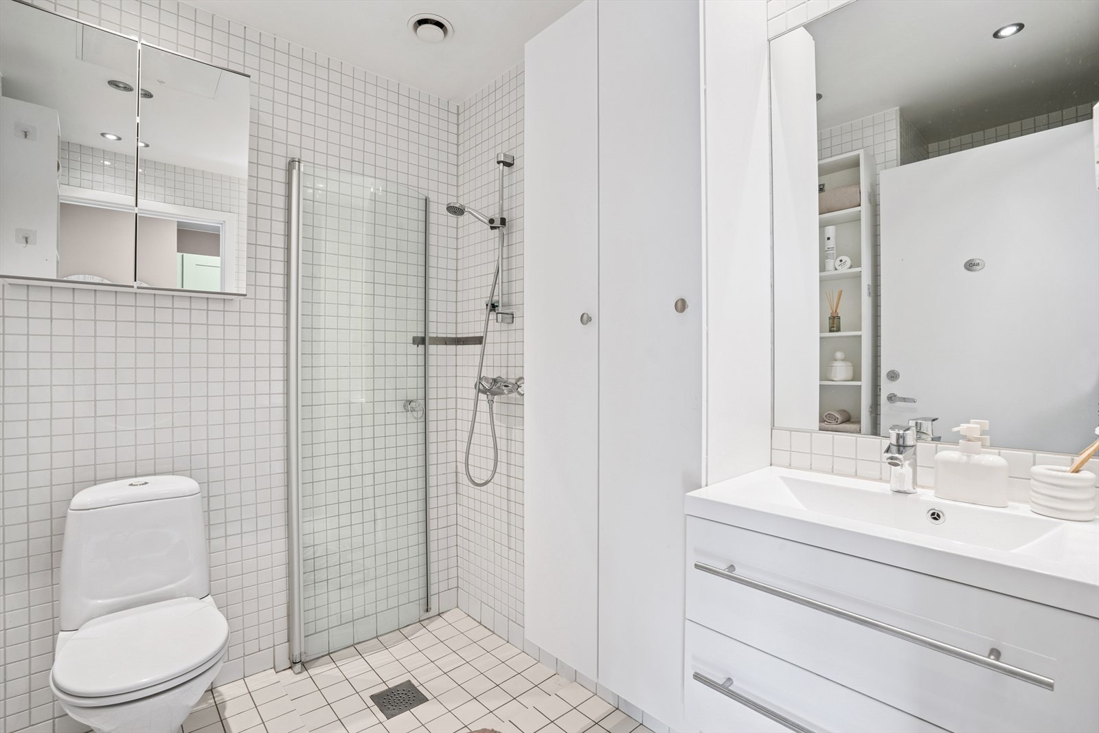 Innredningen består av heldekkende servant med underskap, speil, to høyskap, hyller samt gulvsatt klosett og dusj med svingbar glassvegg. Galleribilde