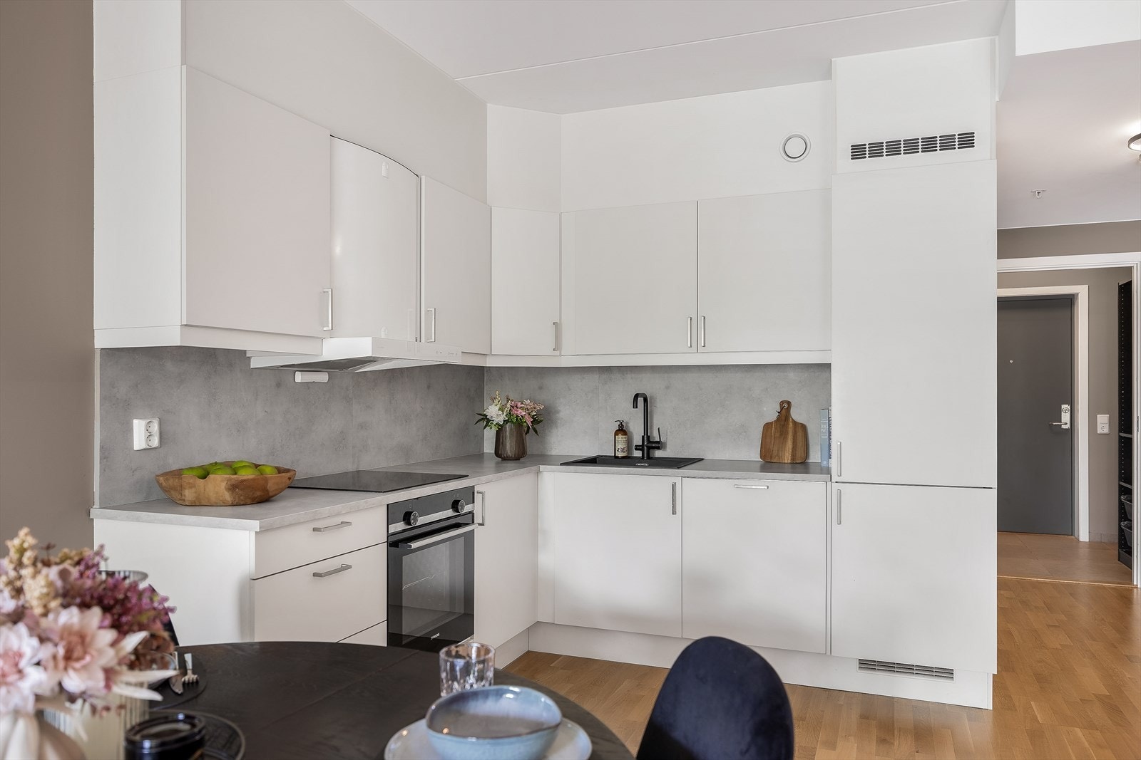 Kjøkkeninnredning med hvite, glatte fronter og lys benkeplate med laminatbelegg. Det er kitchenboard mellom benkeplate og overskap. Galleribilde