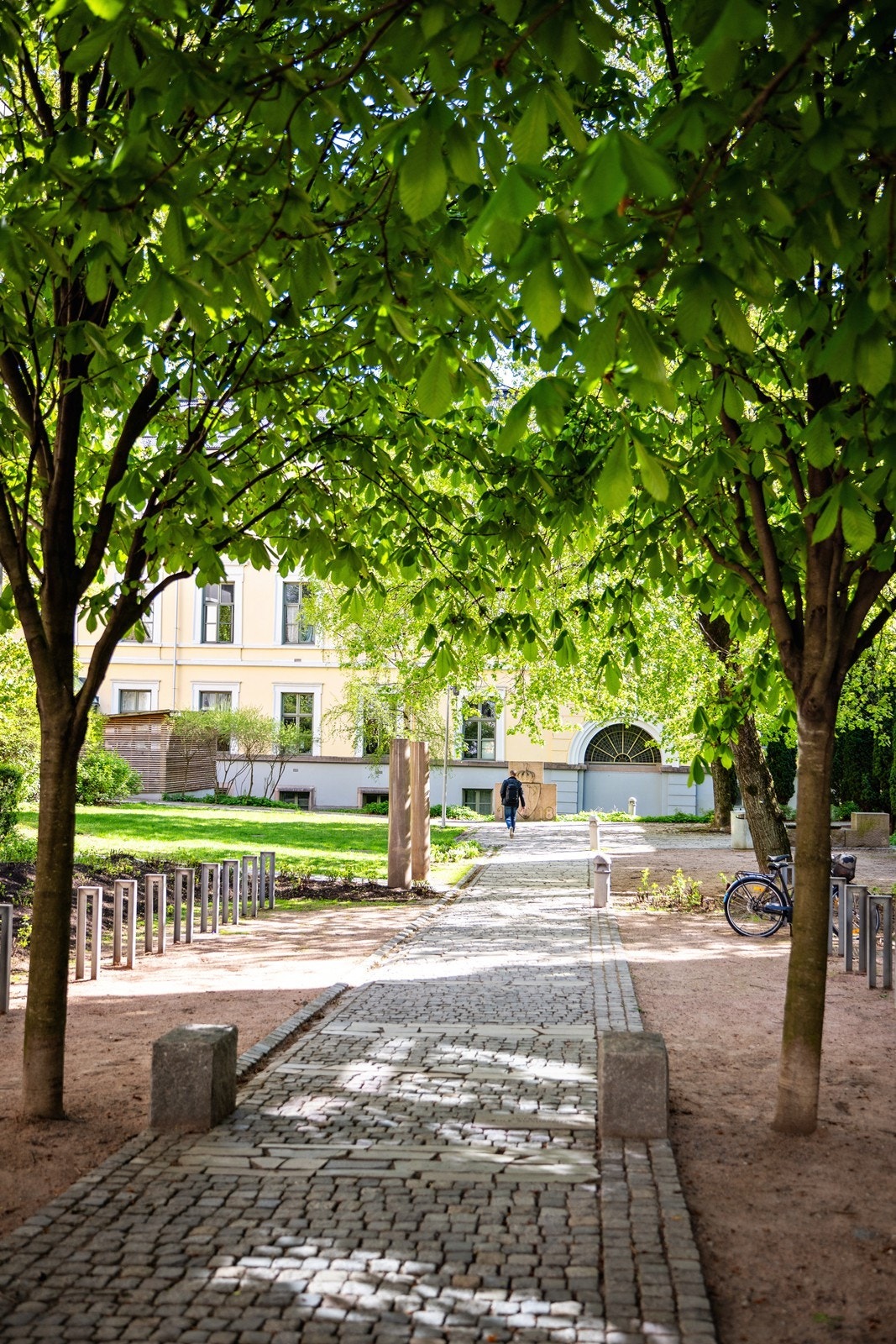 Bakgården har sykkelparkering, brostein og rød sand. Galleribilde