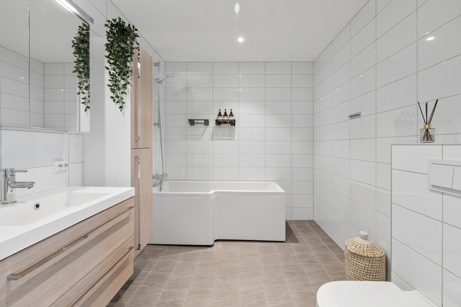 Nøytralt, flislagt baderom utstyrt med badekar og dusjarmatur. Galleribilde