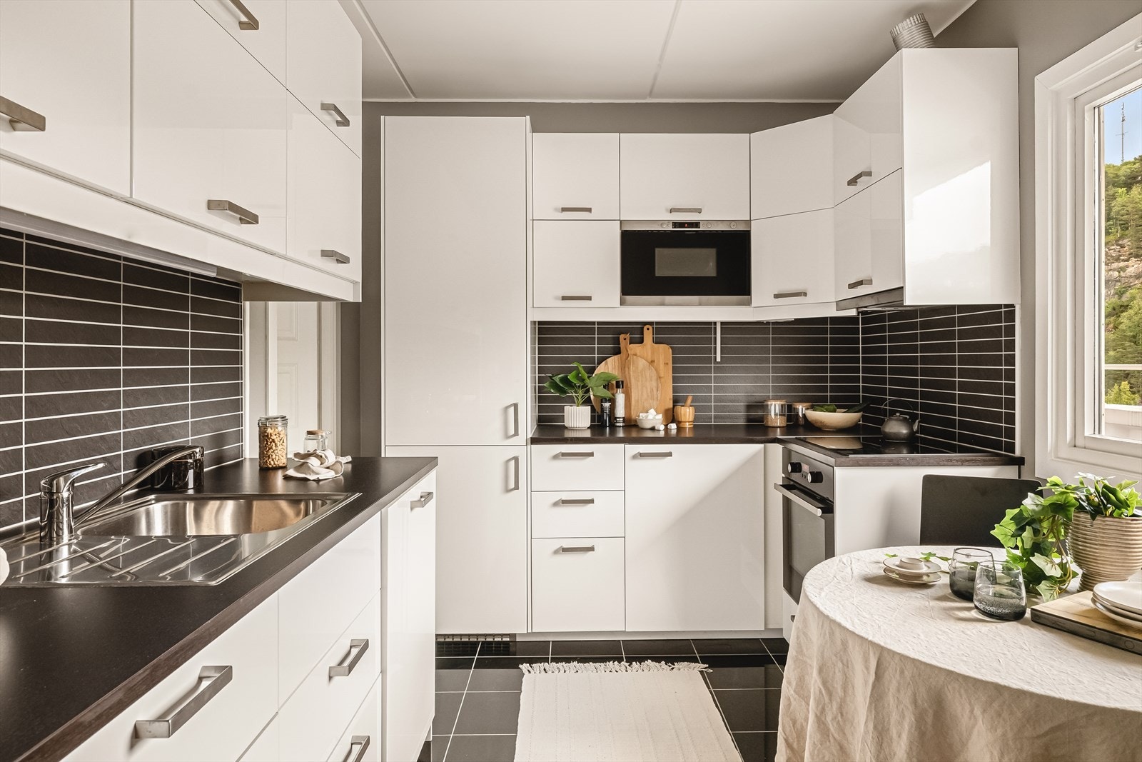 Gulv er flislagt med tøffe sorte fliser, som fortsetter sømløst videre inn på kjøkkenet rett ved inngangspartiet. Galleribilde