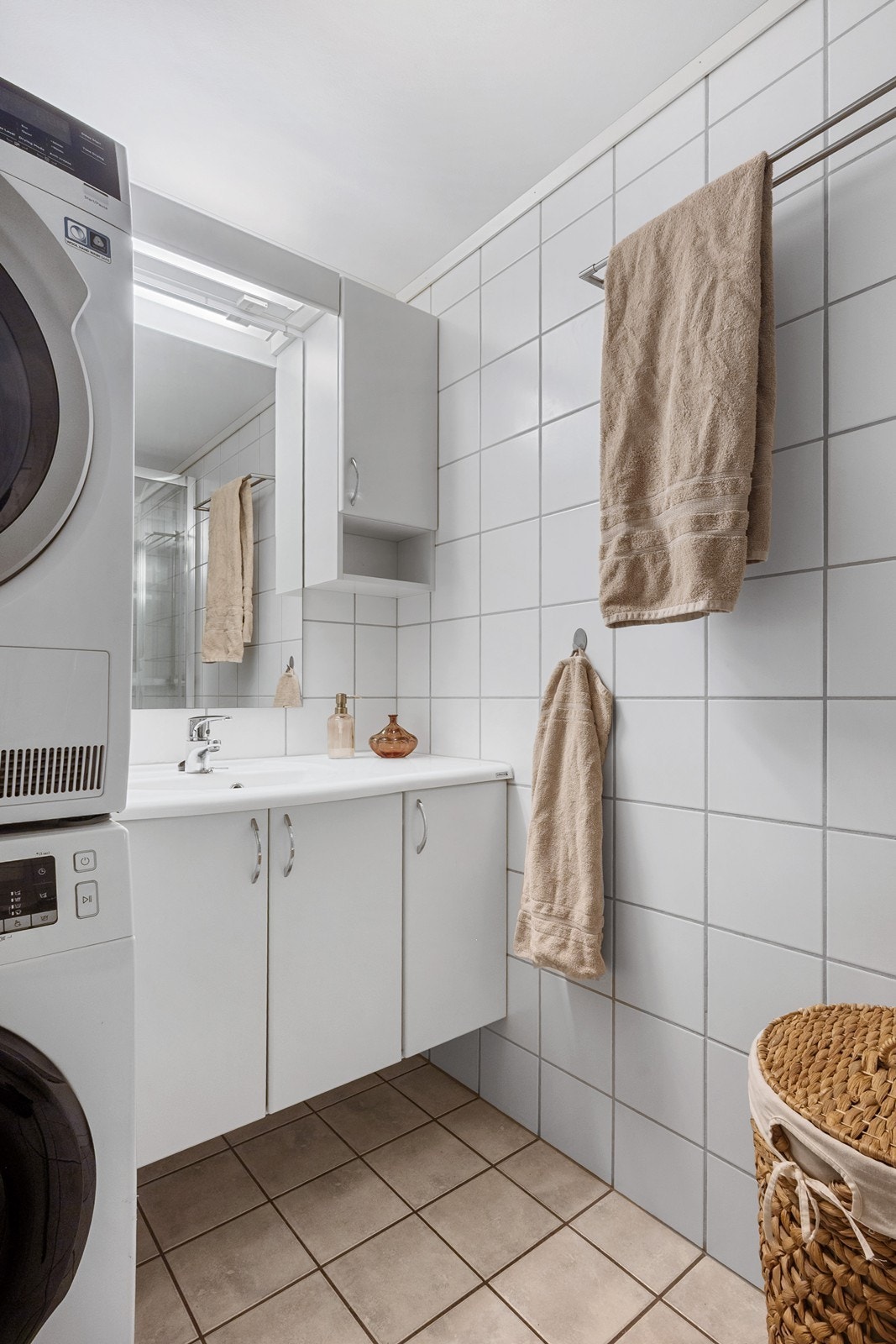 Badet fremstår tidløst med flislagte overflater og gulvvarme, plass til vaskesøyle og servantskap med god oppbevaring. Galleribilde