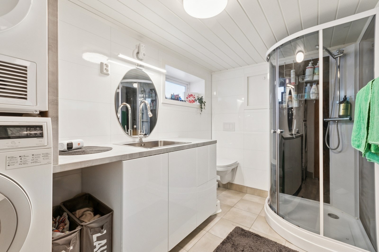 Lyst bad/vaskerom med flislagt gulv og varmekabler. Utstyrt med dusjkabinett, vegghengt wc og smart vaskeromsinnredning. Galleribilde