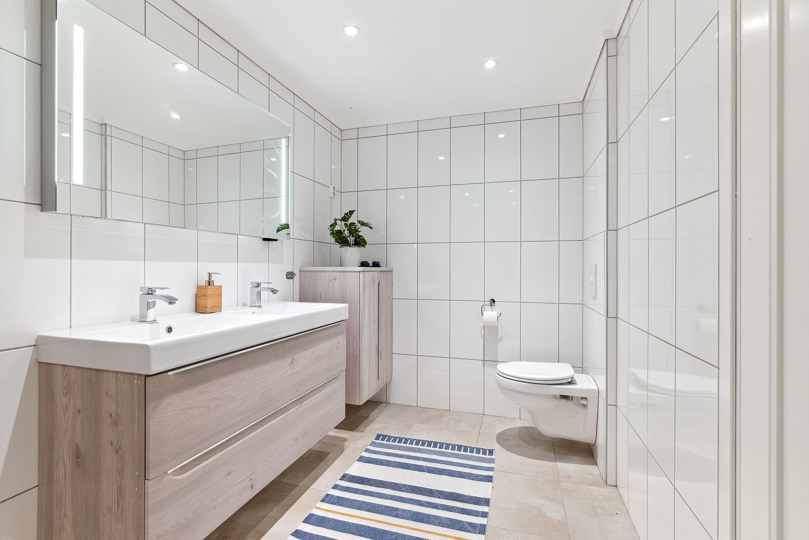 Badet er innredet med stor dusj, vegghengt toalett og dobbeltservant m/innredning. Galleribilde