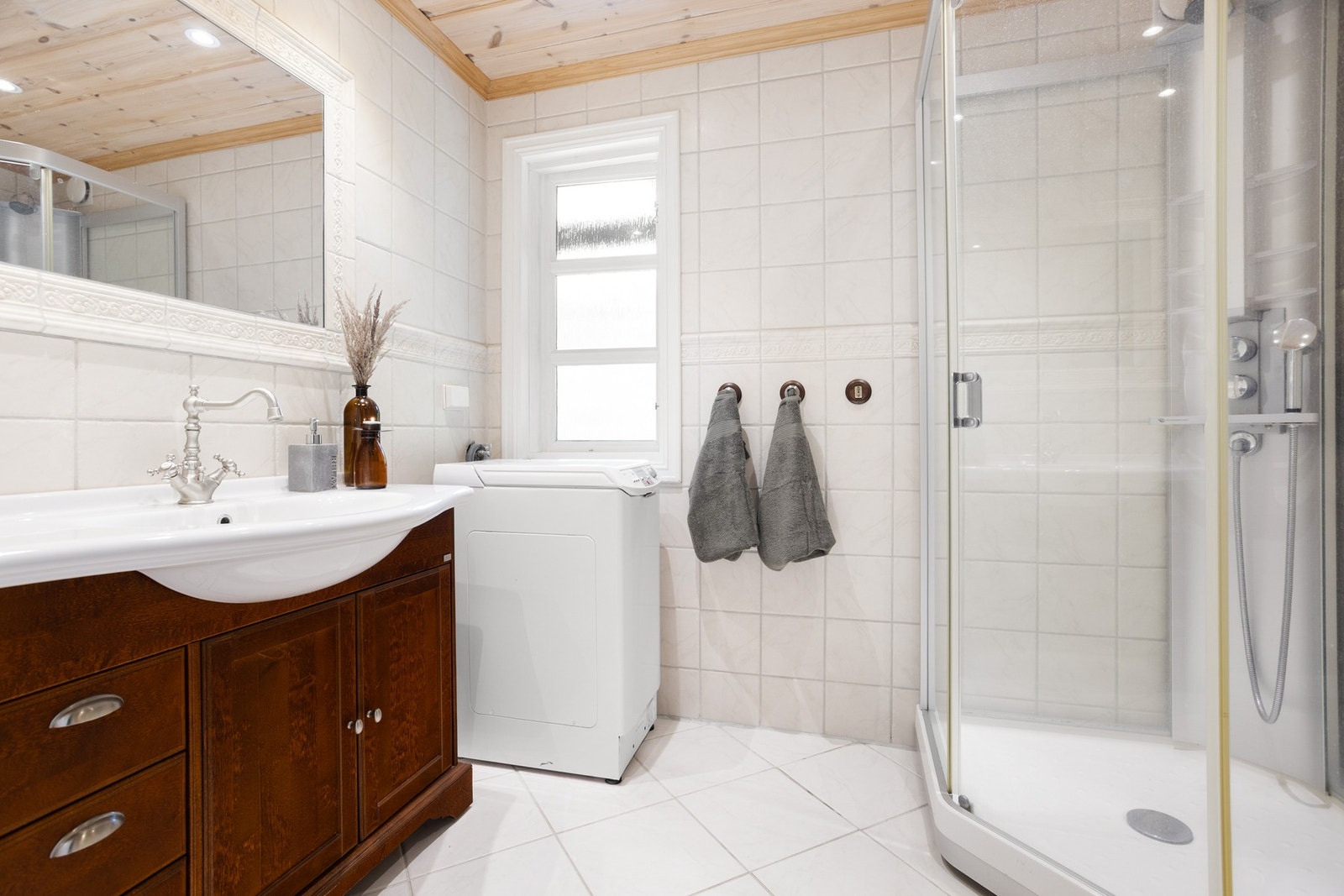 Pent, flislagt bad som er innredet med dusjkabinett, toalett, baderomsinnredning med servant og opplegg for vaskemaskin. Galleribilde
