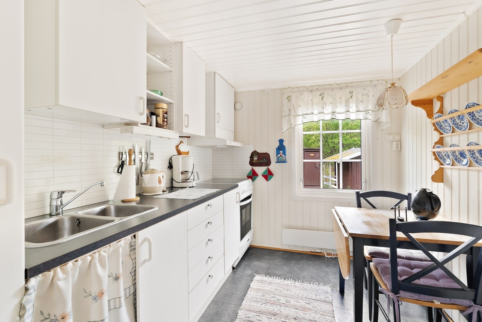 Det er plater med flisemønster på vegg over benk, og ventilator i overskap. Plass for komfyr, kjøleskap og benkeoppvaskmaskin i skap under vask. Galleribilde