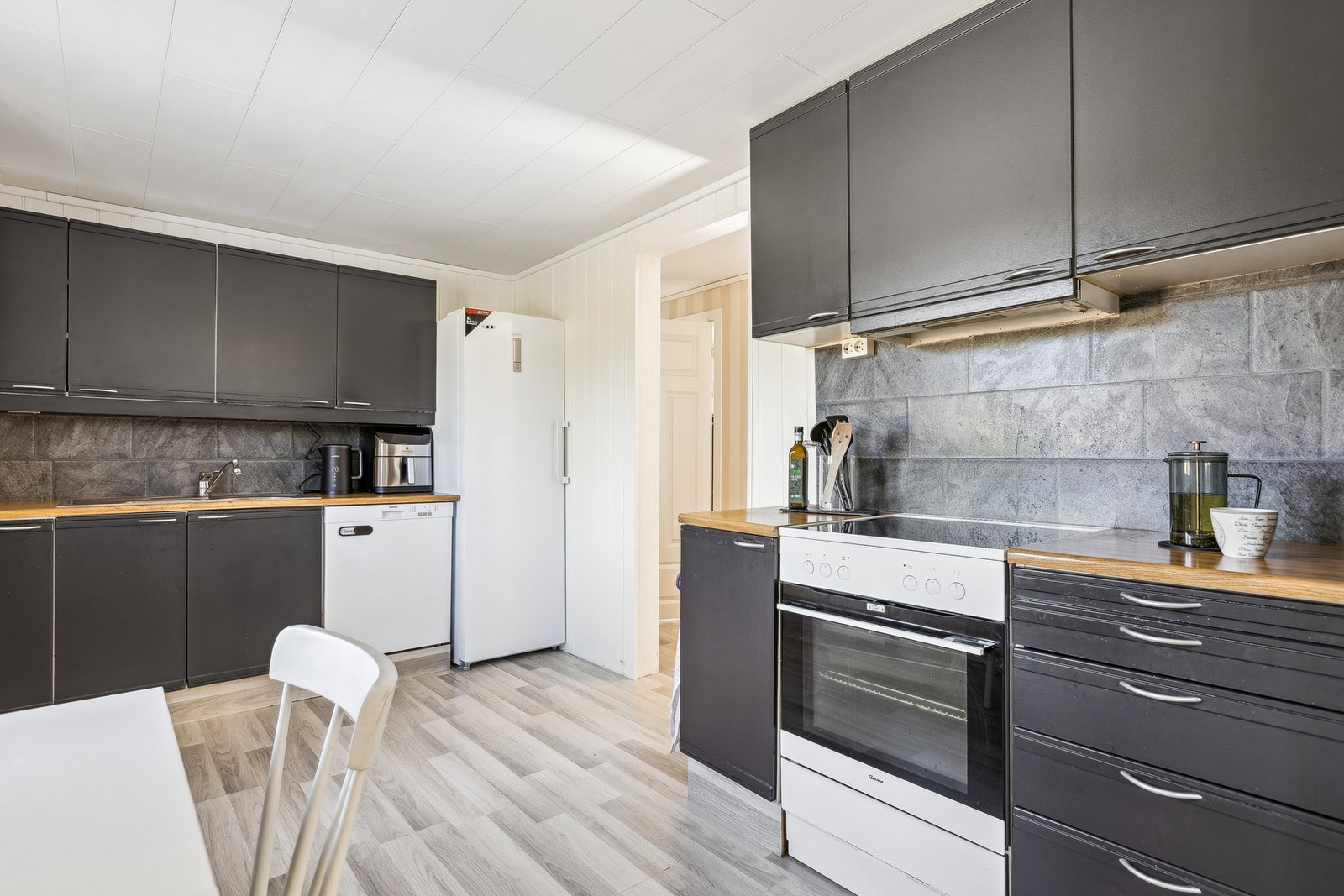 Kjøkkeninnredning med glatte laminat fronter, laminat benkeplate med benkebeslag med to kummer. Avtrekkshette over stekesone. Galleribilde