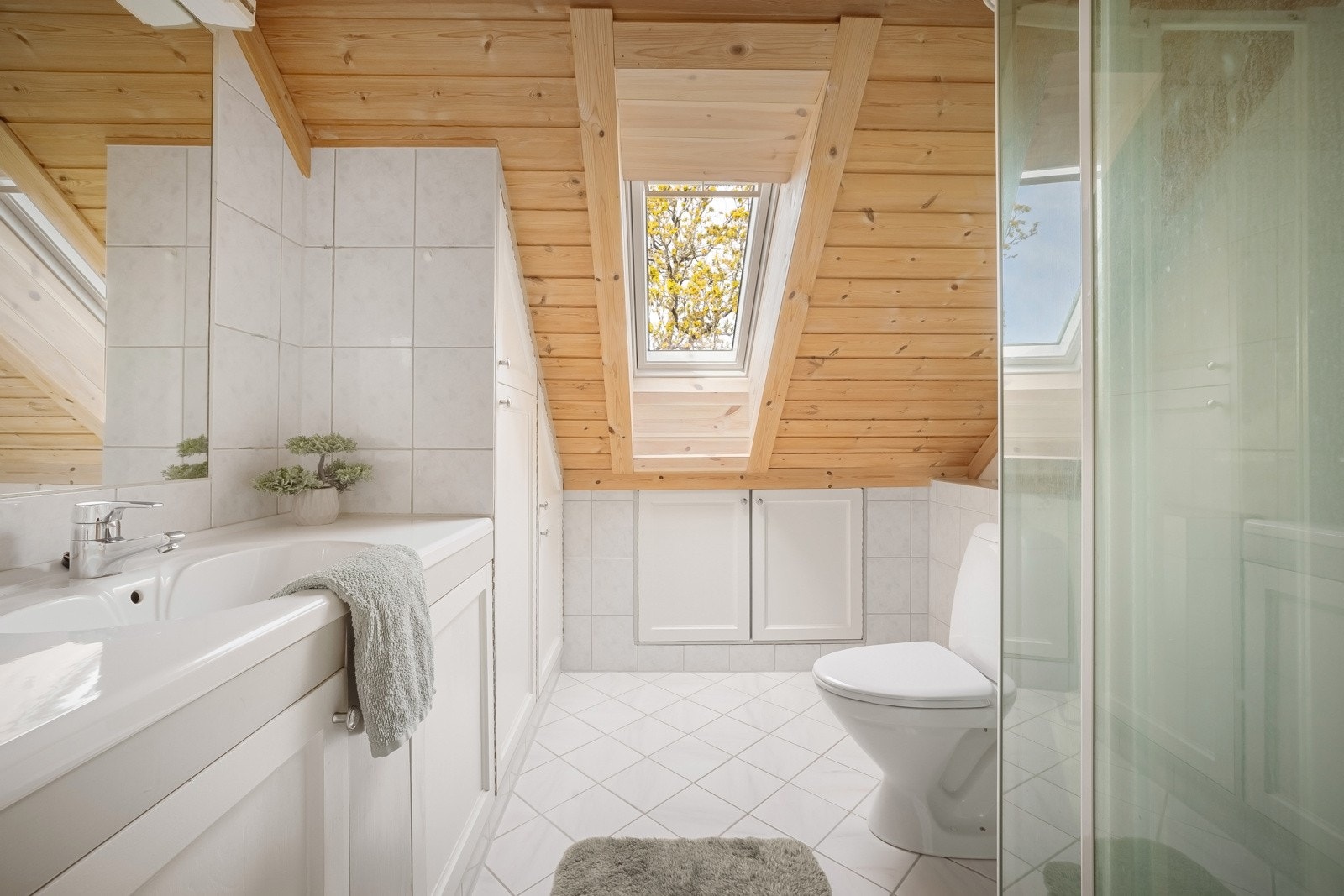 Lyst baderom med fliser på gulv og vegger. Badet er utstyrt med baderomsinnredning med nedfelt servant, dusjkabinett og toalett Galleribilde