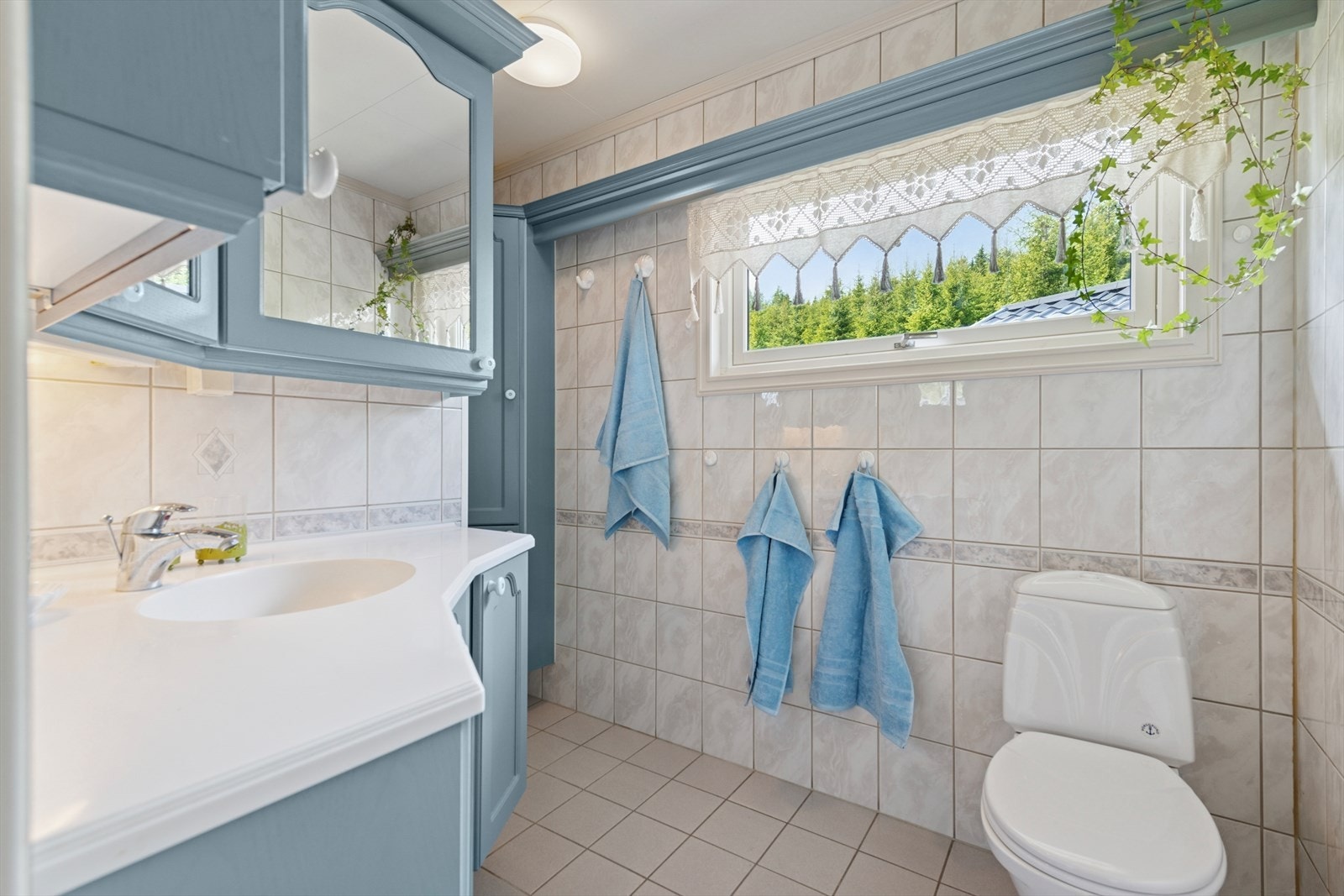 Det flislagte baderommet er utstyrt med gulvstående klosett, dusjsone og servantinnredning med vask og skap. Galleribilde