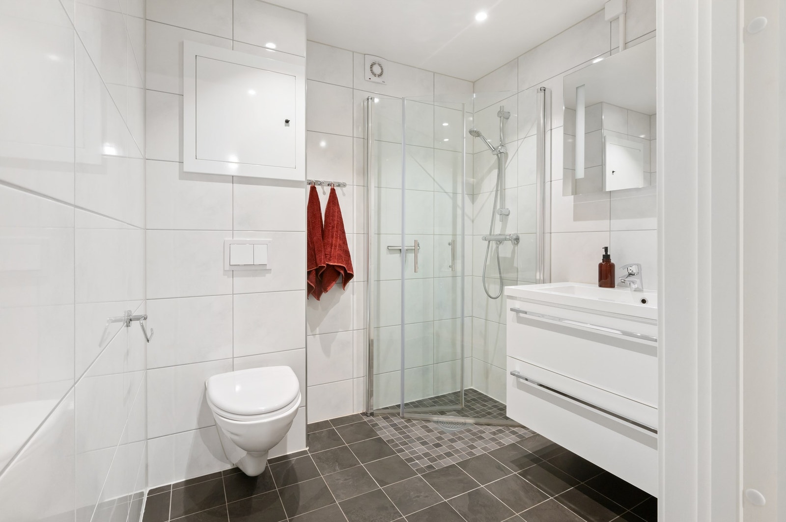 Badet inneholder servantskap med ovenpåliggende servant med ett-greps blandebatteri og speil, dusjhjørne med innfellbare glassdører, vegghengt toalett og varmtvannsbereder. Galleribilde